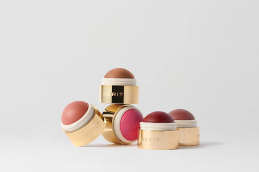 Merit lip balm sticks in various shades including pink, red, and brown, arranged in a small pyramid on a clean white background.