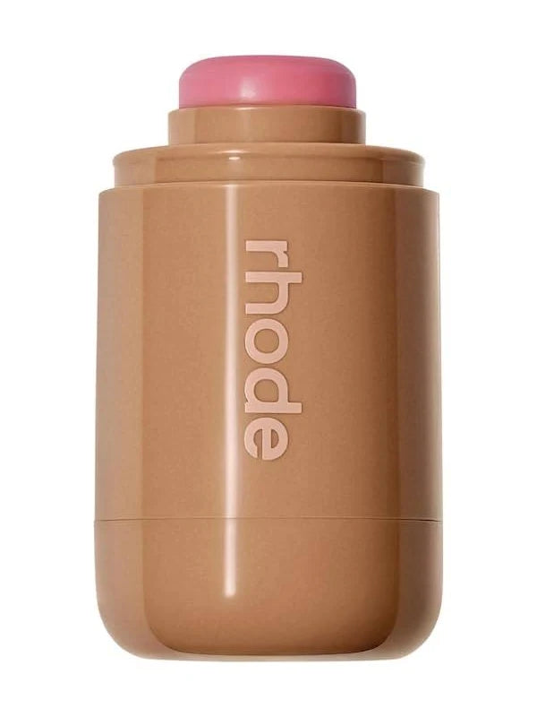 A cylindrical makeup stick container in a warm tan-brown shade with a pink cap, featuring the brand name 'rhode' printed vertically in white on the front, set against a plain white background.