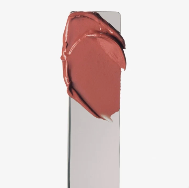A close-up of a cream blush or lipstick swatch applied on a clear rectangular spatula, showing a warm dusty rose color, against a plain white background.