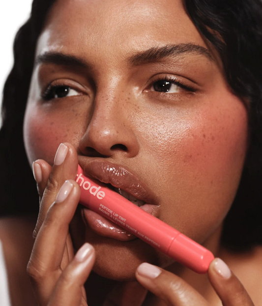 A close-up of a woman holding a pink lip product near her lips, with the brand name 'mode' visible on the tube.