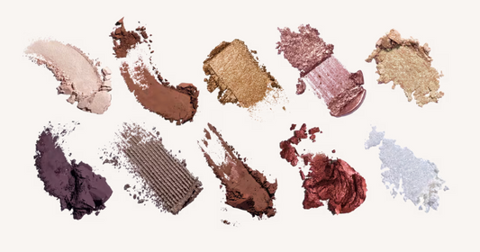 Ten textured eyeshadow swatches in various shades and finishes, including shimmers, mattes, and powders, arranged on a clean off-white background.