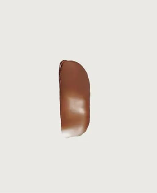 A glossy, elongated vertical smear of medium brown cosmetic cream or liquid on a solid off-white background.